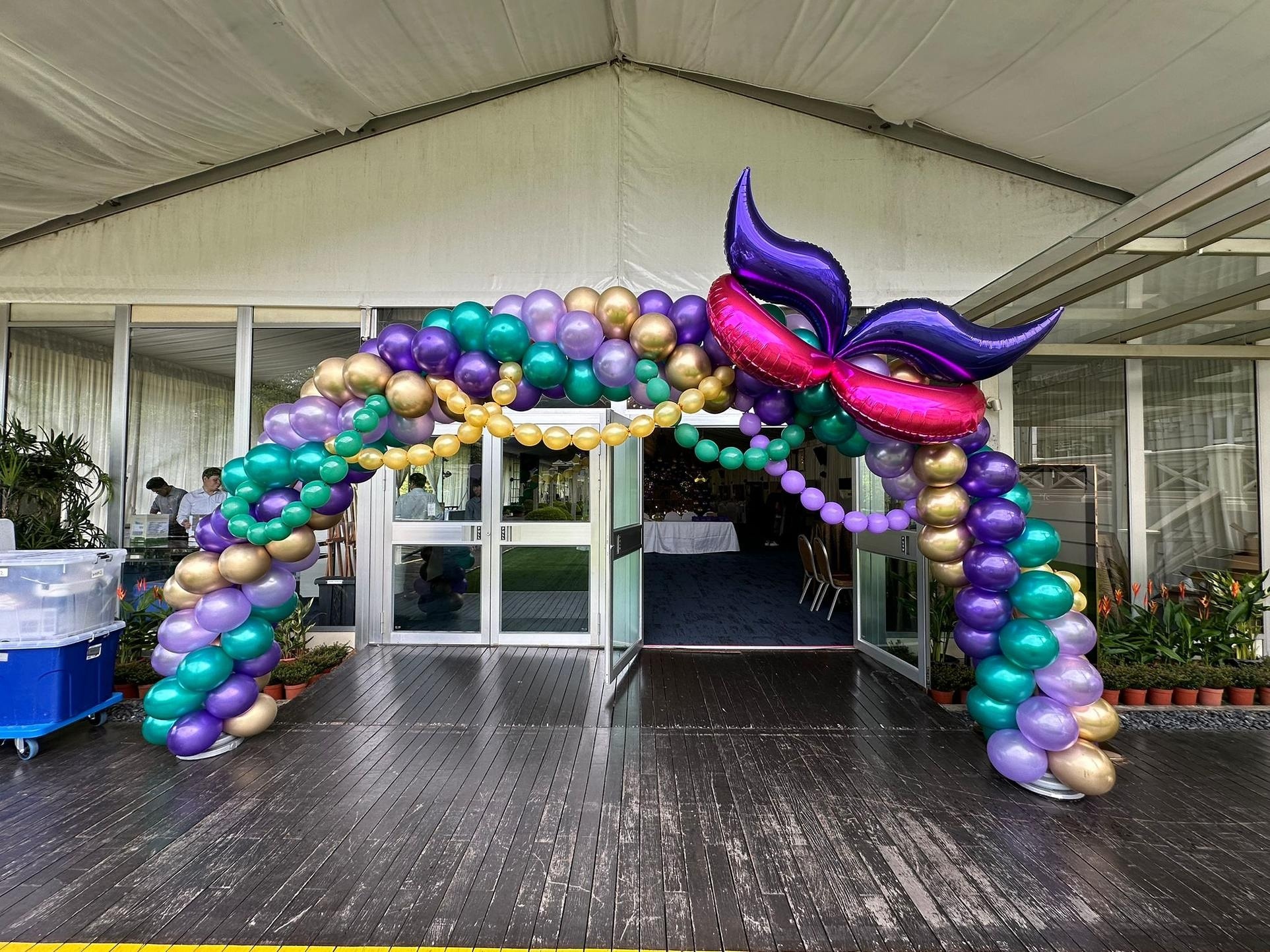 Purple and gold masquerade balloon arch with a large mask detail