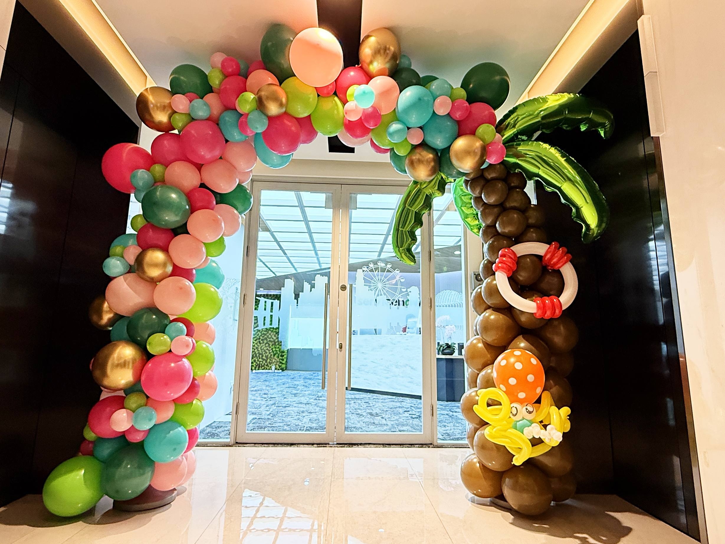 Tropical balloon arch with a palm tree beside glass doors
