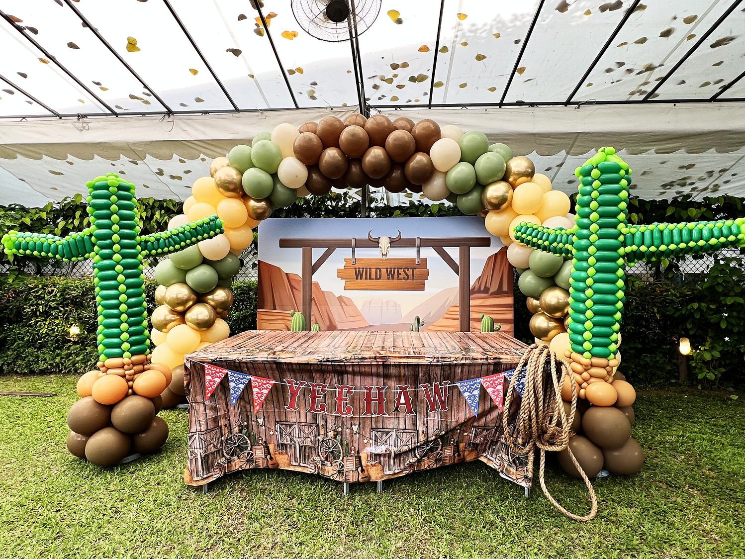 Western themed balloon arch with cactus sculptures and a display table