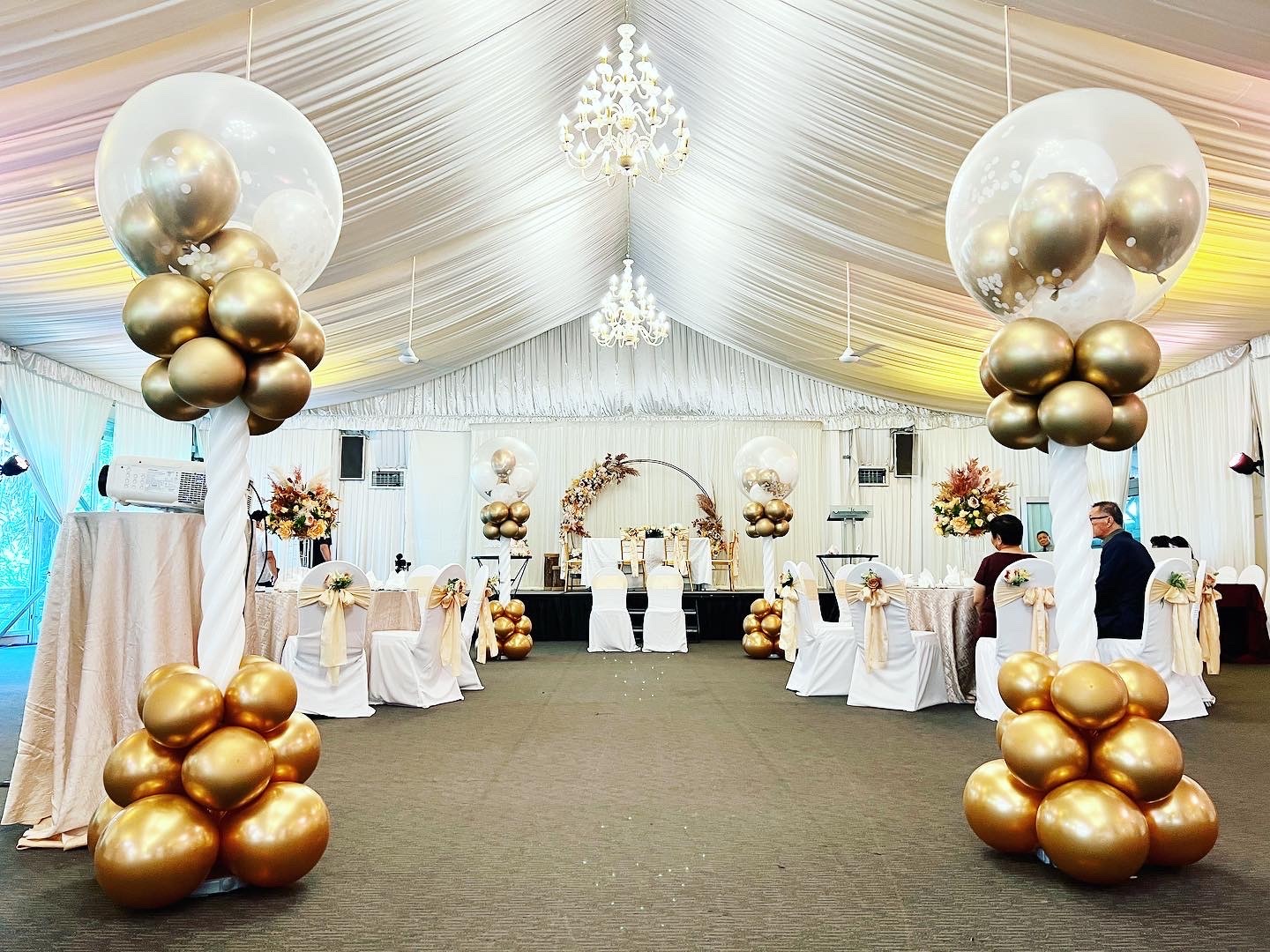 Gold and white balloon pillars framing a wedding marquee entrance