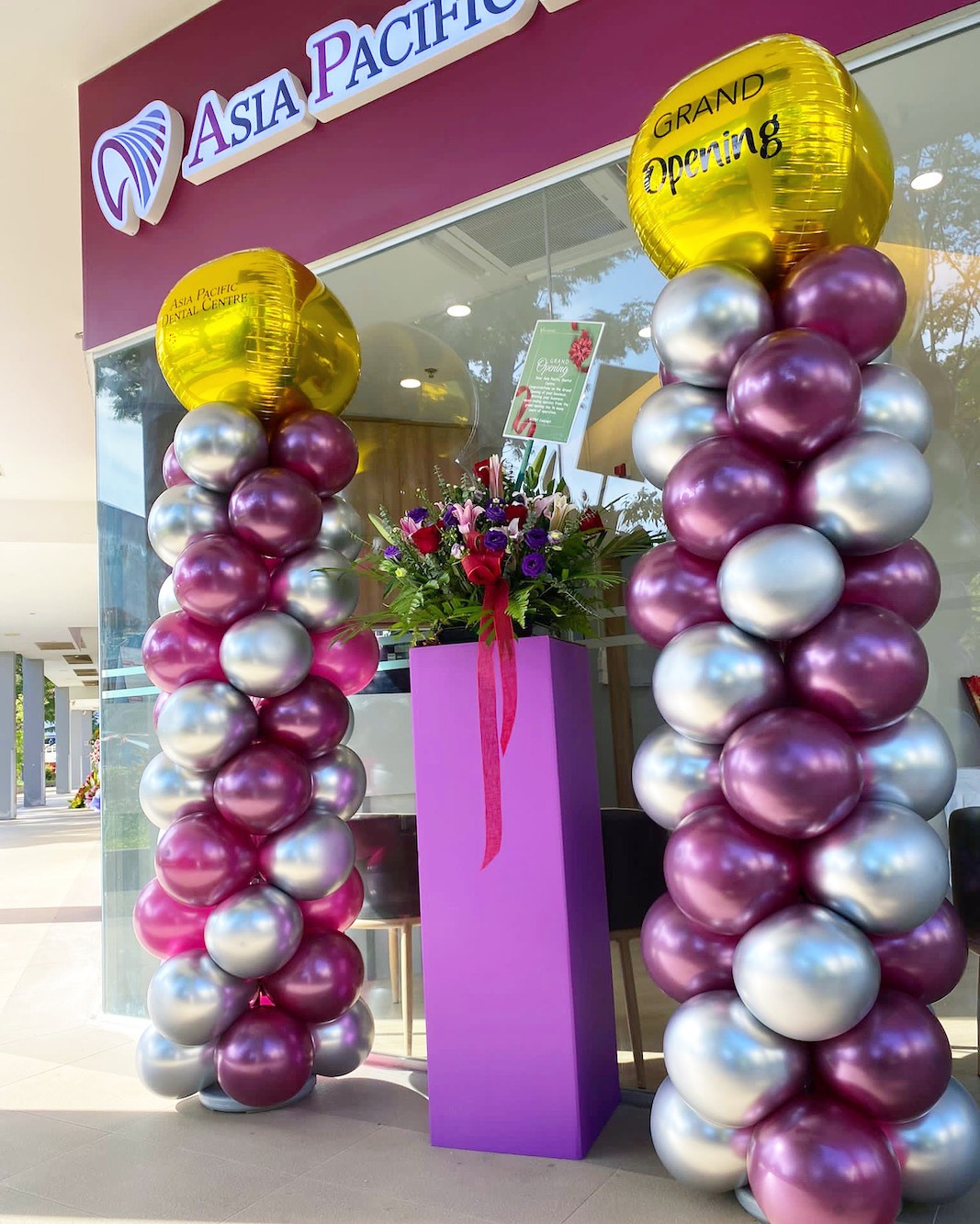 Purple and silver balloon pillars with gold grand opening toppers