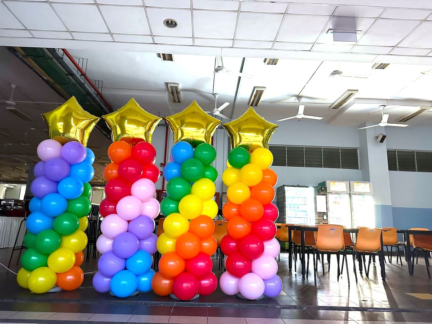 Four rainbow spiral balloon columns with gold star toppers