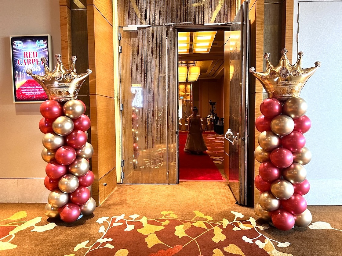Red and gold crown-topped balloon pillars at open ballroom doors