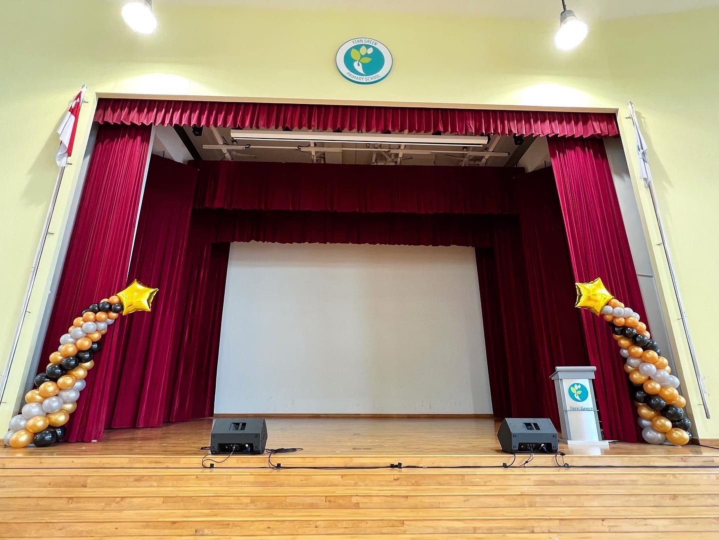 Black and gold star-topped balloon columns beside a school stage