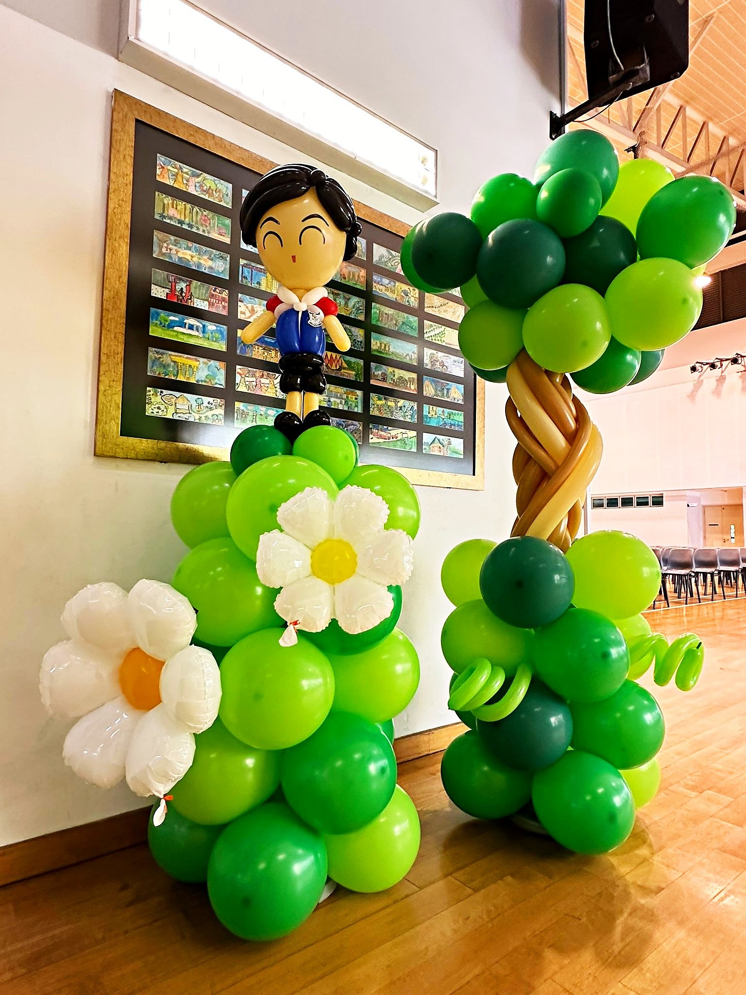 Schoolboy balloon figure beside a tree and flowers