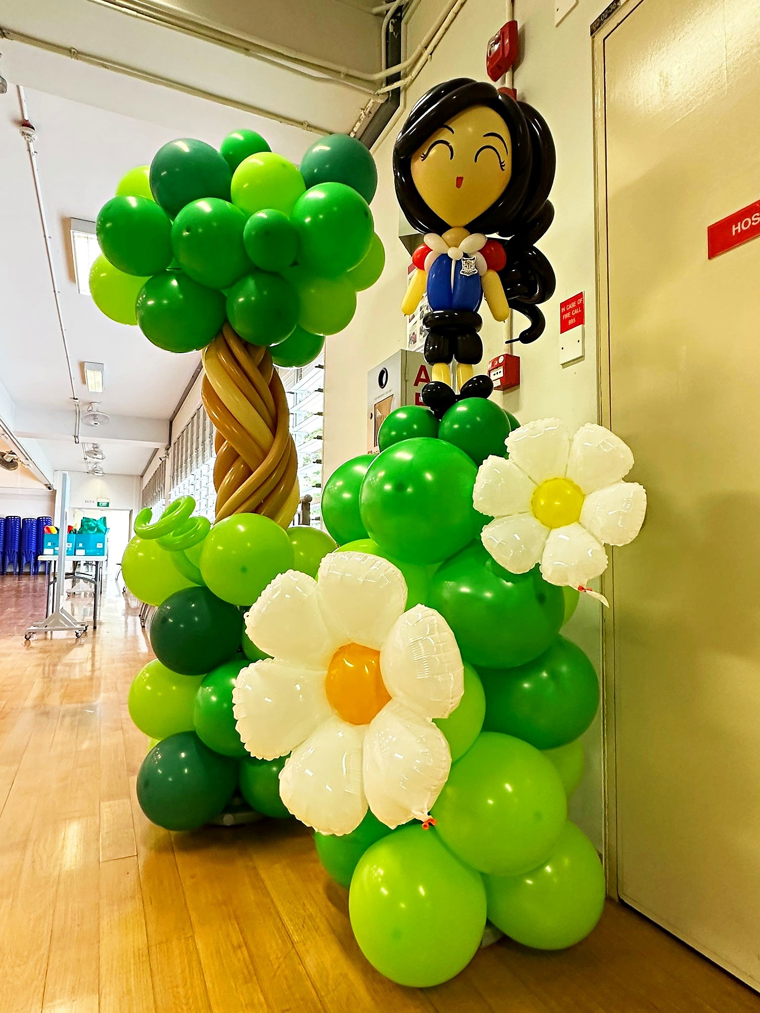 Schoolgirl balloon figure beside a tree and flowers